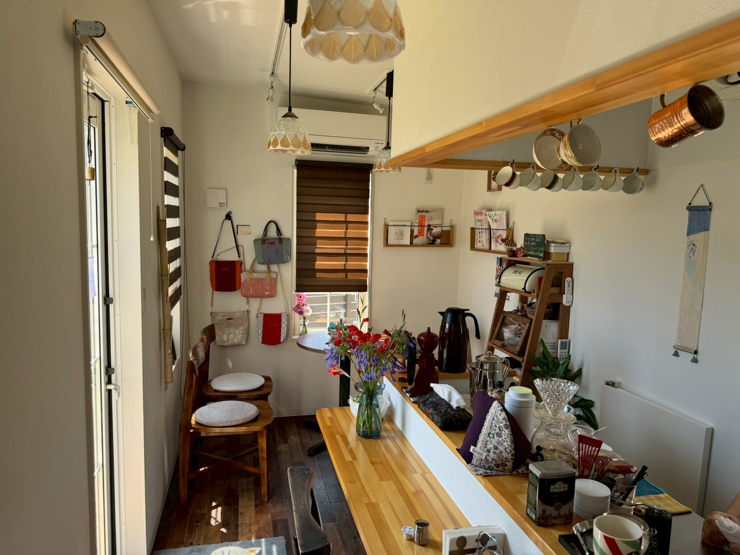 ペンダントライトが優しく灯るトレーラーハウス内装。カウンターに季節の花、壁には手づくりのバッグ、カップが並ぶカフェ空間